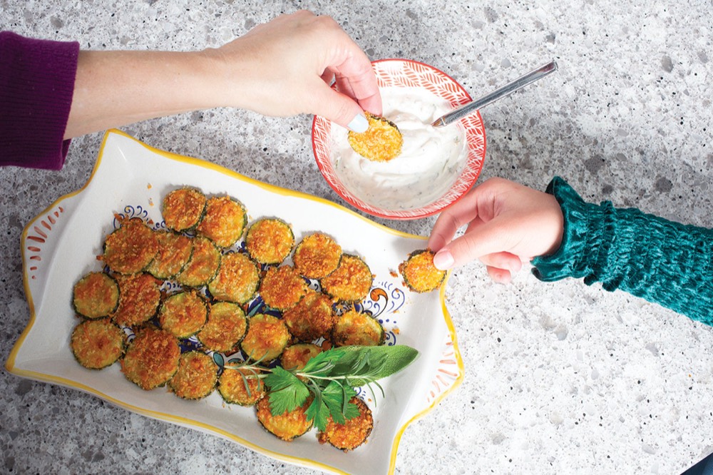 Hands dipping a zucchini crisp into yogurt dip